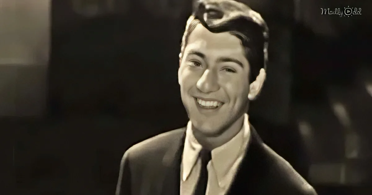 A smiling man in a suit and tie, with a blurred background, appears in a black-and-white image.