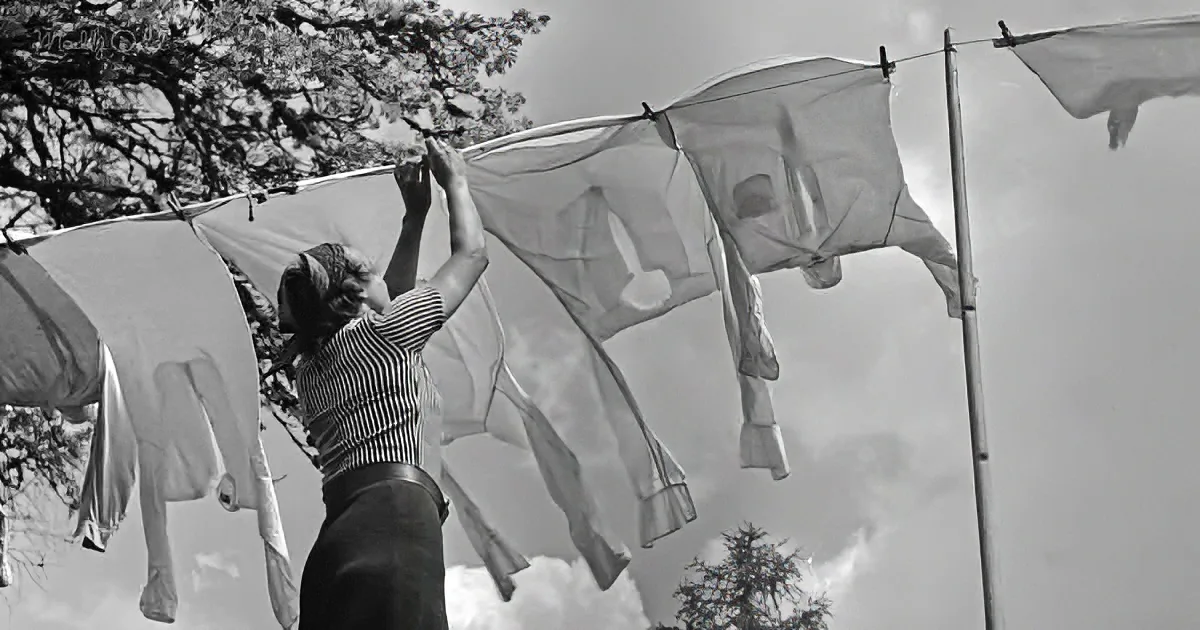 A woman hangs laundry on a clothesline under a cloudy sky.