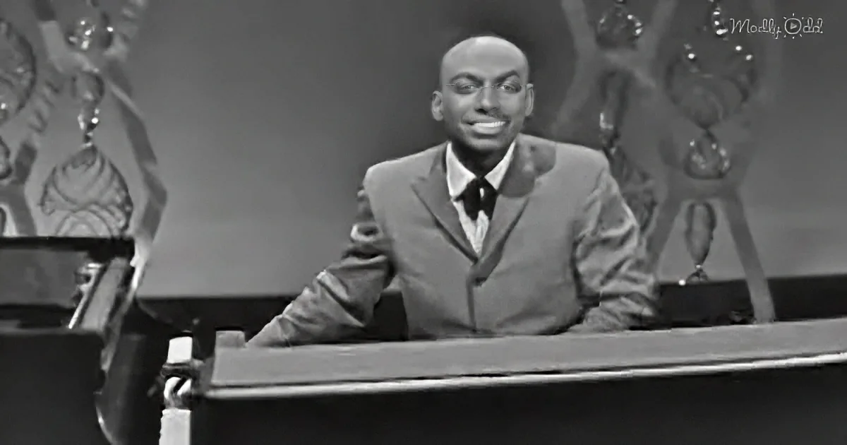 A man in a suit sits at a desk, smiling, with a decorative background.