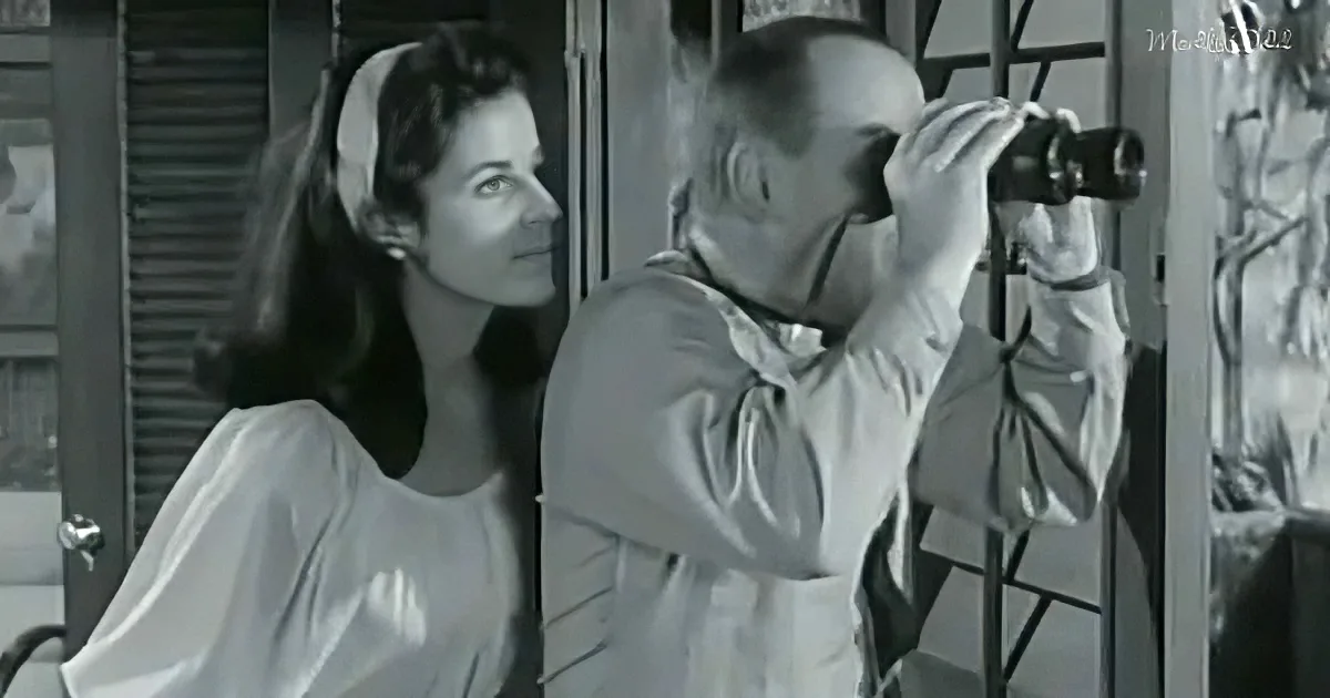 A woman in a white dress looks on as a man in a white lab coat uses binoculars.