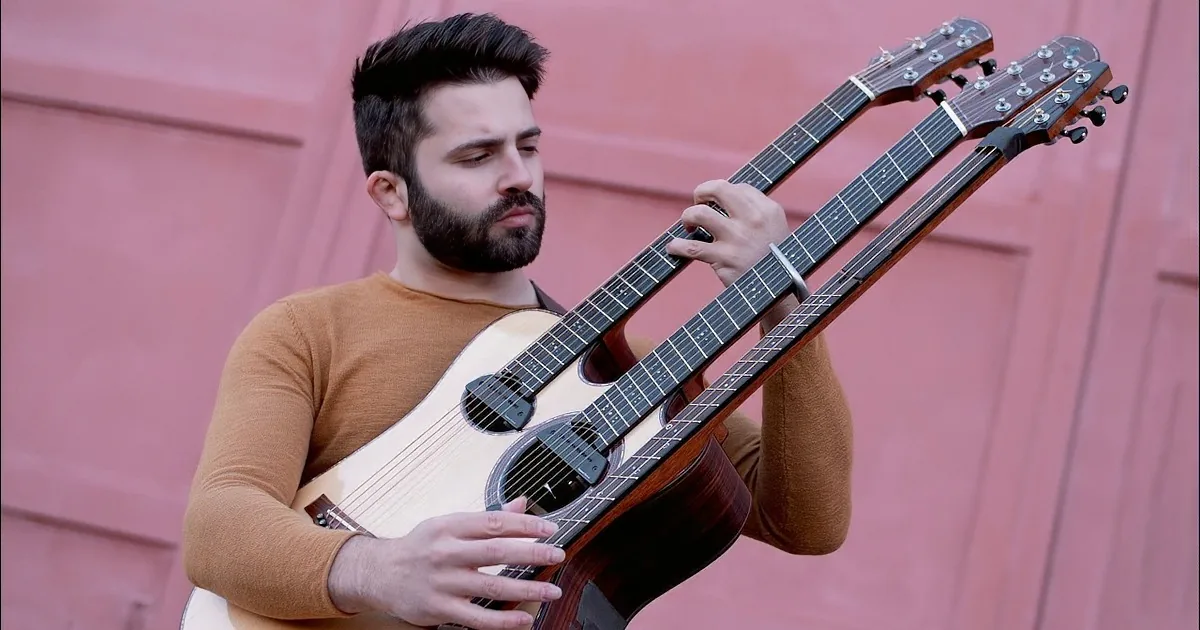 A man plays a multi-neck guitar against a pink door.