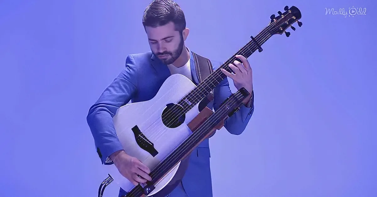 A man in a blue suit plays a white guitar against a purple background.