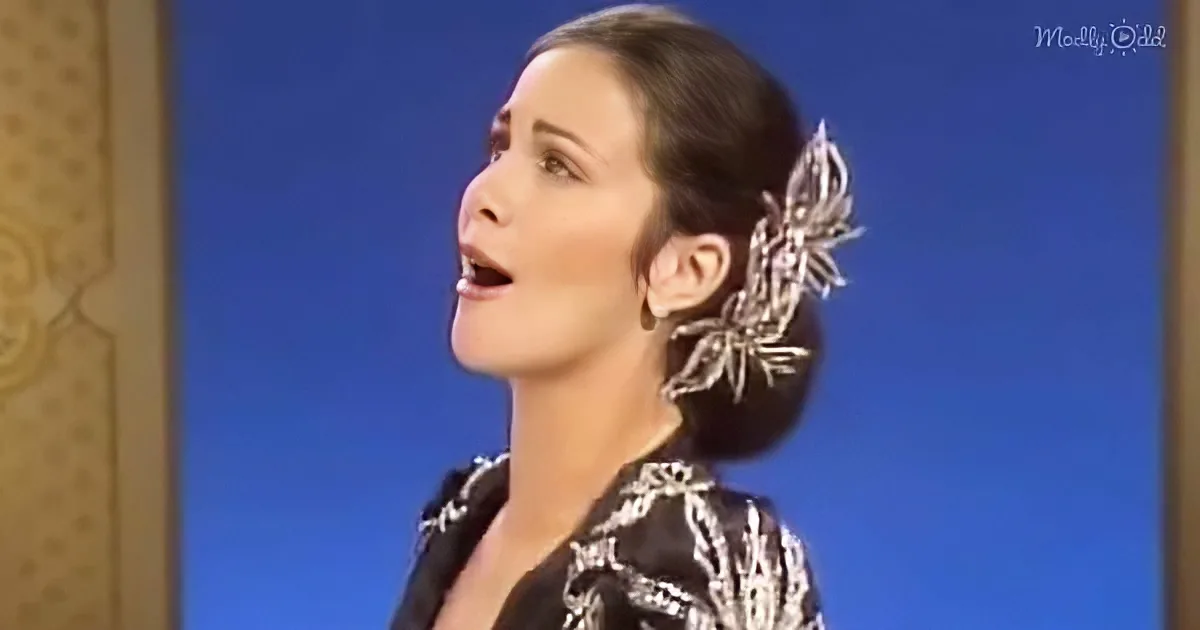A woman in a black and white patterned outfit with a large silver earring and a blue background.