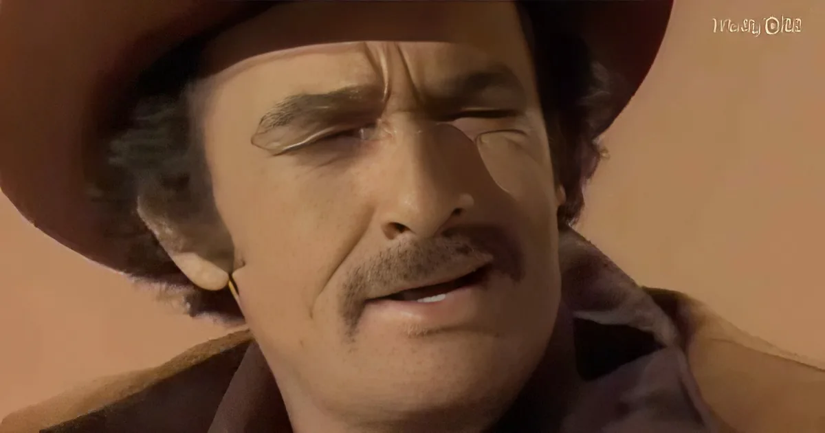 A man in a cowboy hat and brown shirt, eyes closed, mouth slightly open, against a beige background.