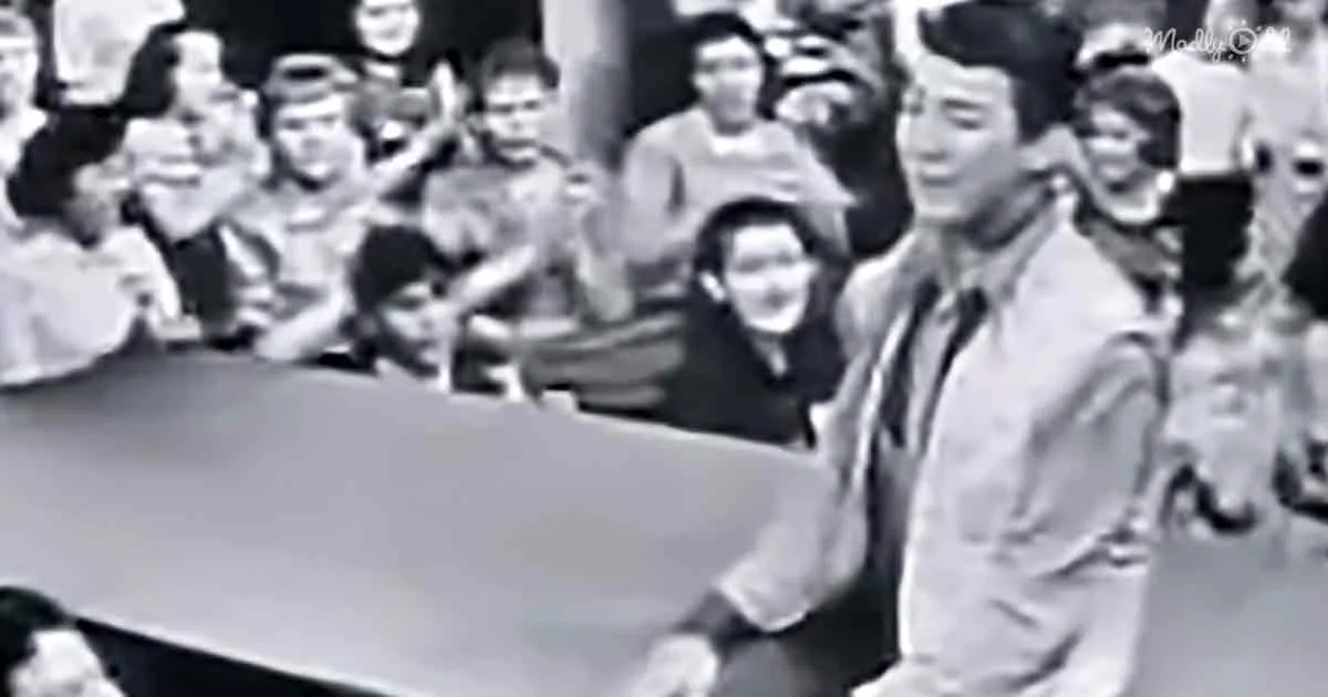A man in a suit and tie is standing in front of a crowd, possibly giving a speech or presentation.