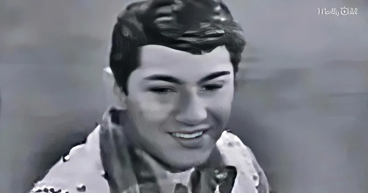A smiling young man with short, styled hair and a button-up shirt is the main subject.