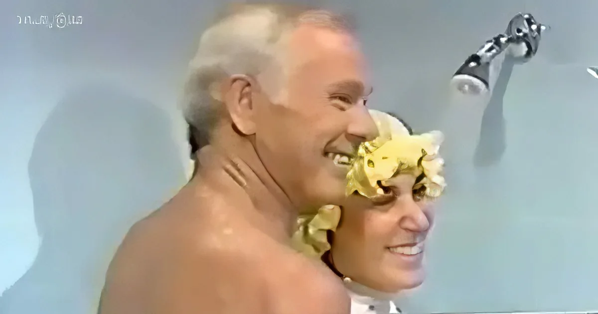 A man and woman are in a shower, both smiling, with flowers covering the woman's face.