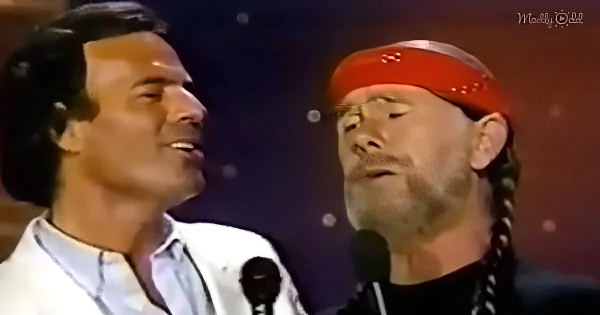Two men singing, one in white shirt, the other in black with red bandana, both holding microphones.