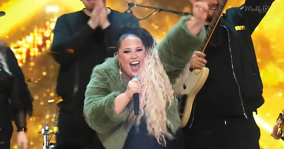 A woman in a green fur coat sings passionately into a microphone on stage with a band.