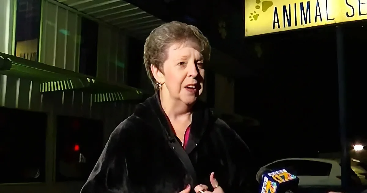 A woman in a black jacket stands outside at night, speaking near an "Animal Services" sign.