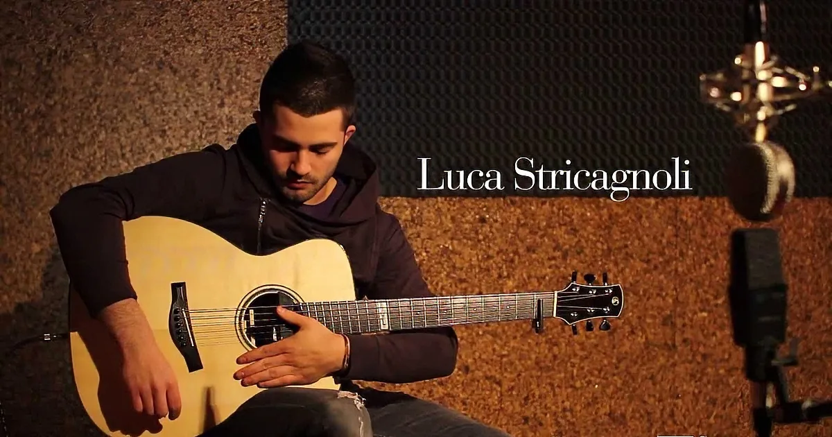 A man in a hoodie plays an acoustic guitar in a dimly lit room with soundproofing.