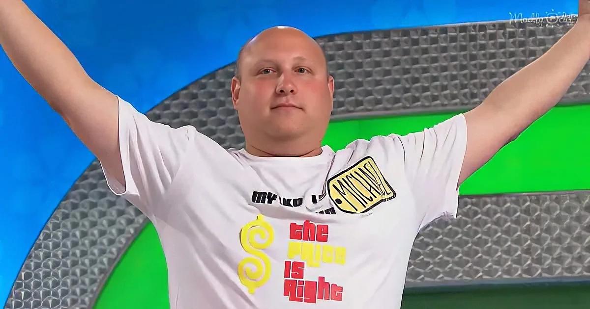 A man in a white "The Price is Right" t-shirt raises his arms in celebration against a blue and green background.