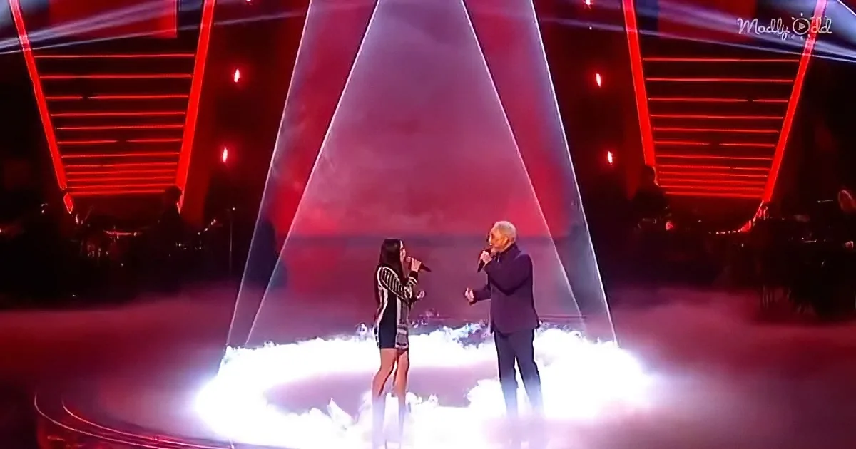 A woman and man sing on a stage with red lighting and smoke.