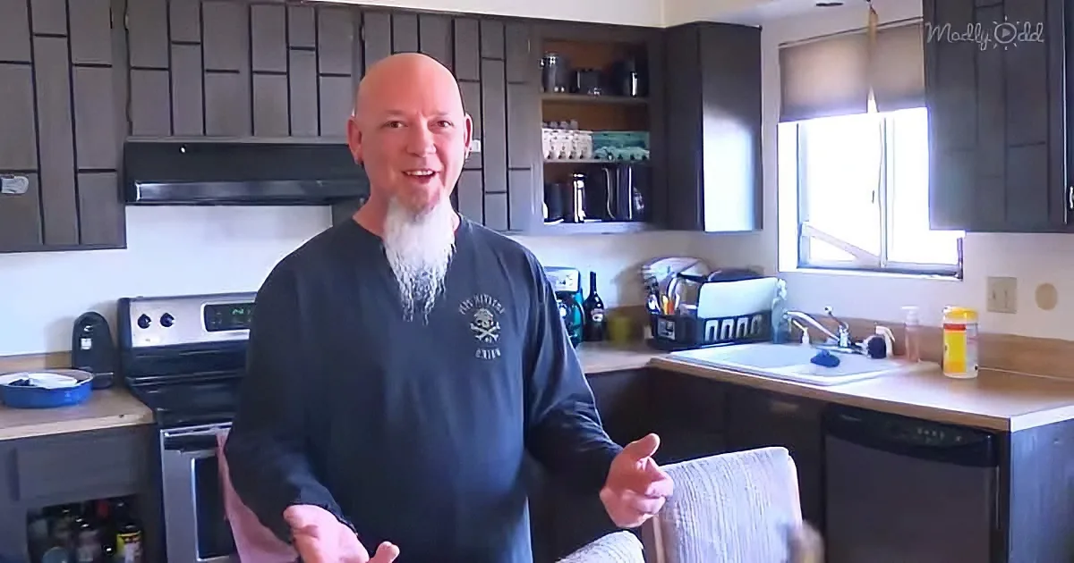 A man with a white beard and bald head stands in a kitchen, gesturing with his hands.