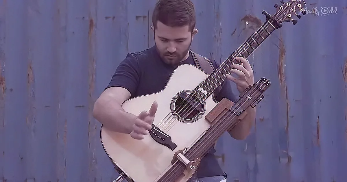 A man plays an acoustic guitar against a weathered blue wall.