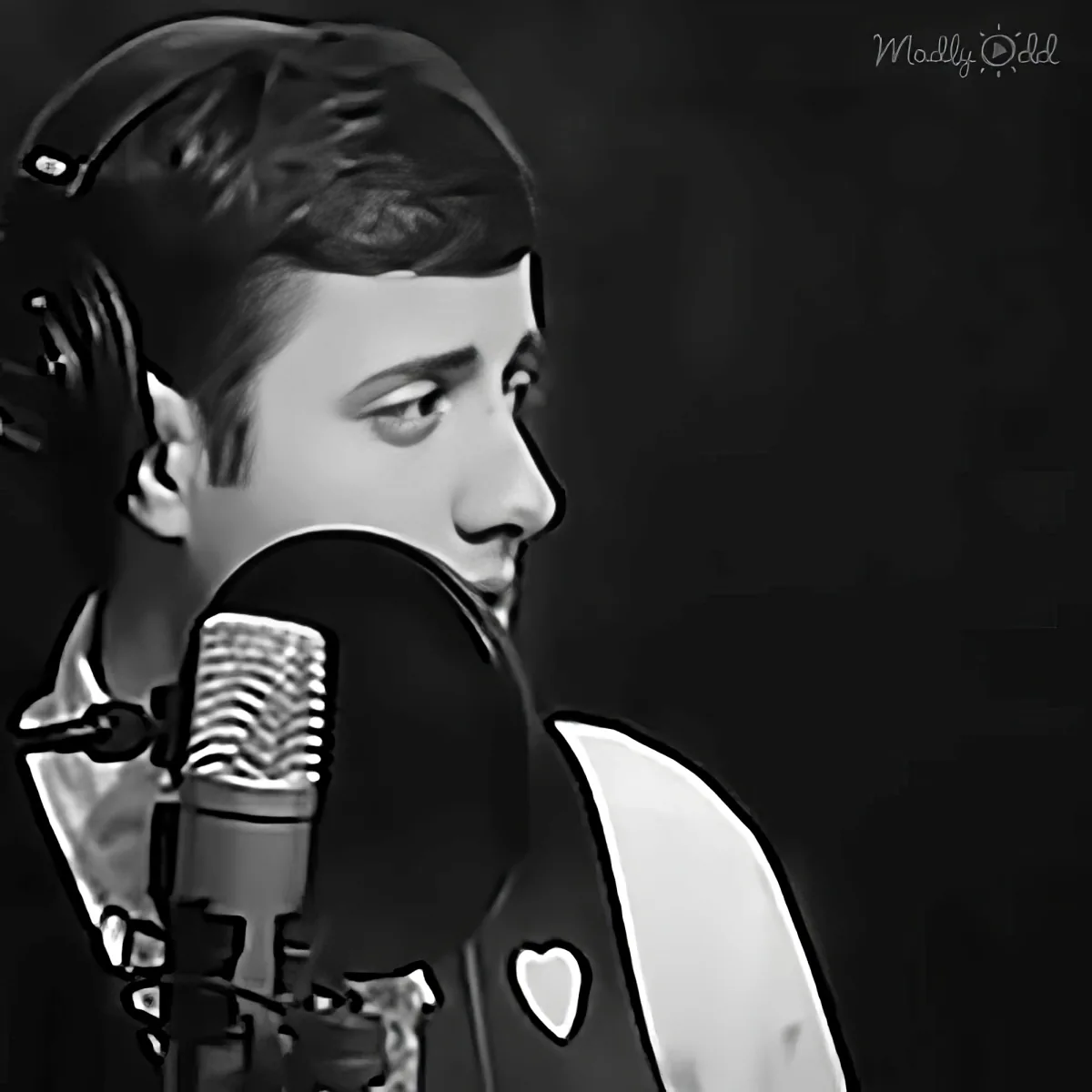 A person wearing headphones and a white shirt with a heart patch sings into a microphone.