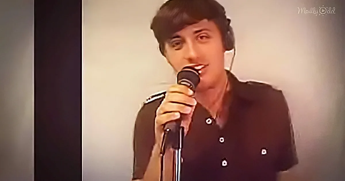 A person in a black shirt holds a microphone, singing into it.