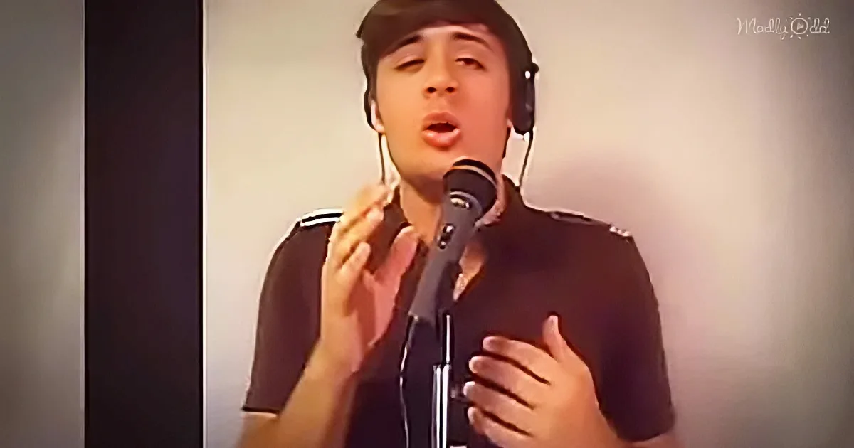 A person wearing headphones sings into a microphone, gesturing with their hands.