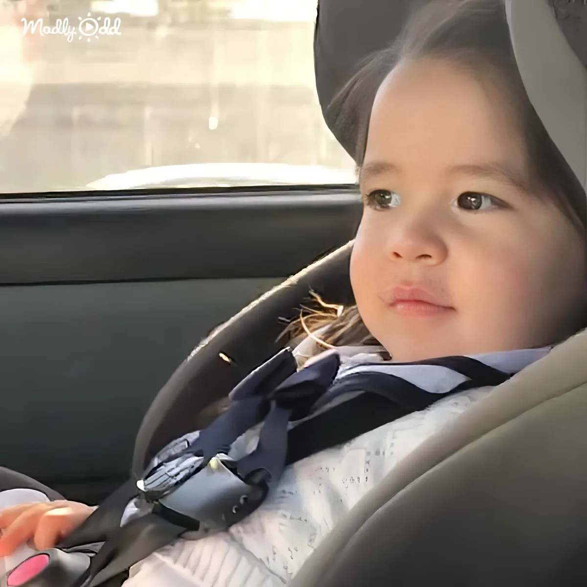 A child in a car seat, wearing a striped shirt, looks up with a curious expression.