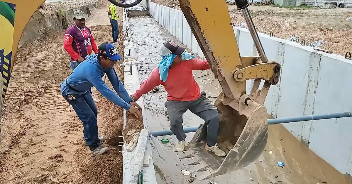 A construction worker is being lifted by an excavator bucket while another worker assists on the ground.