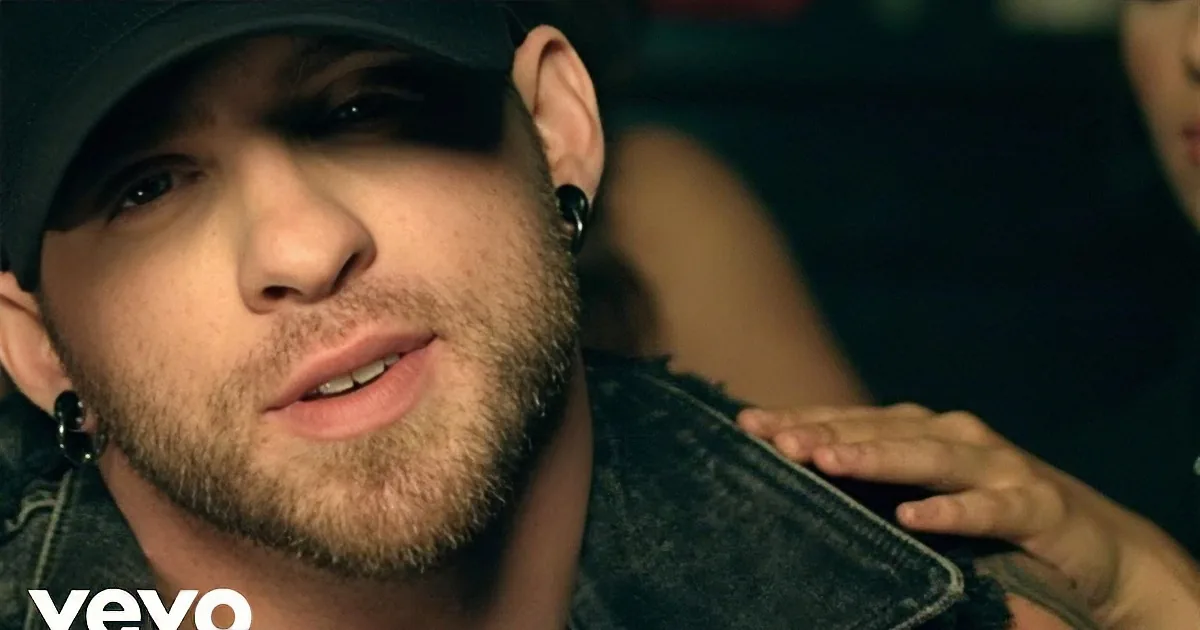 A man with a beard, wearing a black cap and a denim jacket, is seen in a close-up shot.