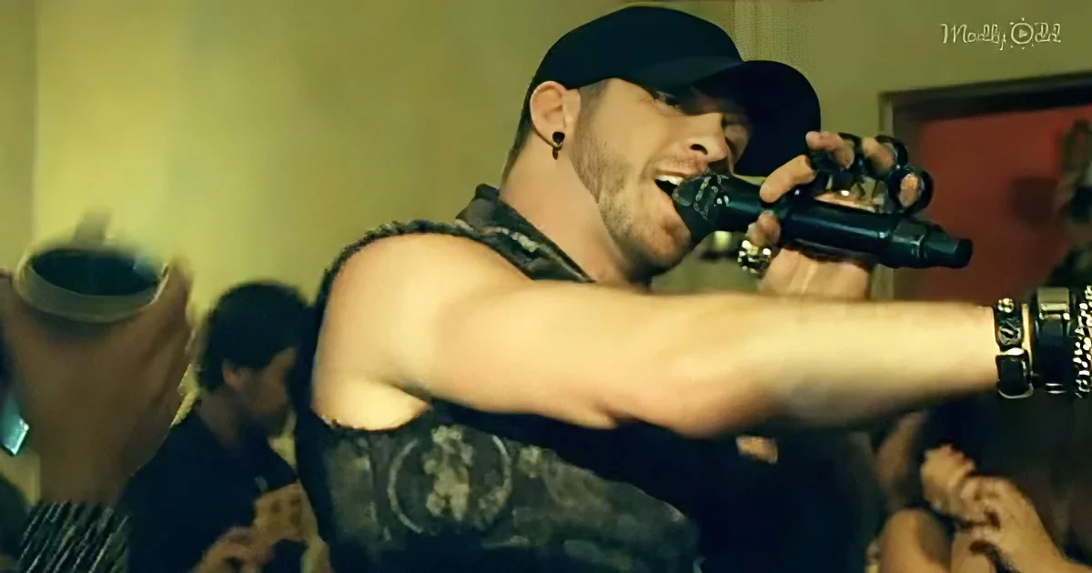 A man in a black cap and vest holds a microphone, singing passionately in front of a crowd.