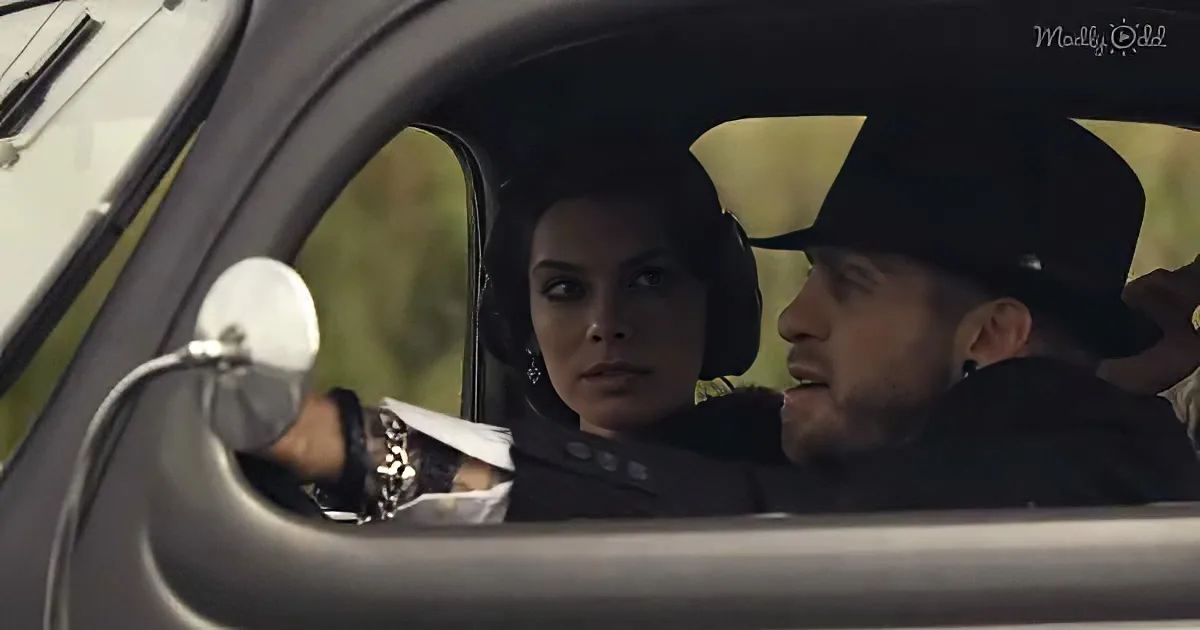 A woman drives a car, looking ahead, while a man in a cowboy hat sits beside her, both focused.