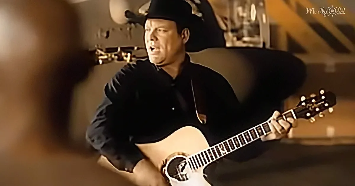 A man in a black shirt and hat plays an acoustic guitar in a dimly lit room.