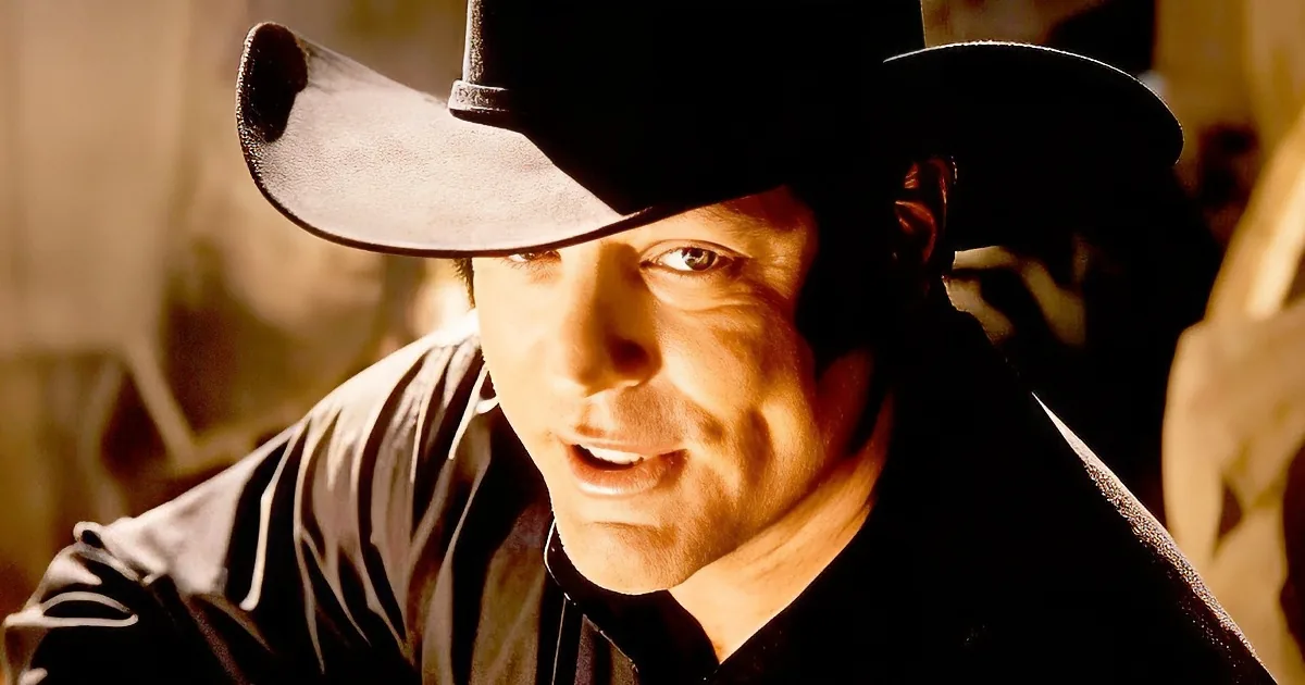 A man in a cowboy hat and dark shirt adjusts his hat, looking intense.