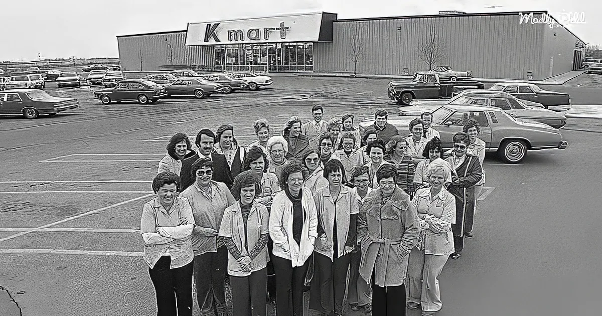 A group of women stands in front of a Kmart store with vintage cars in the background.
