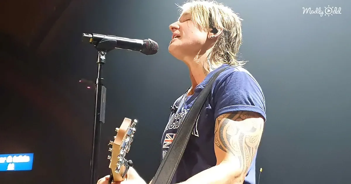 A person with tattoos plays guitar and sings into a microphone on stage.