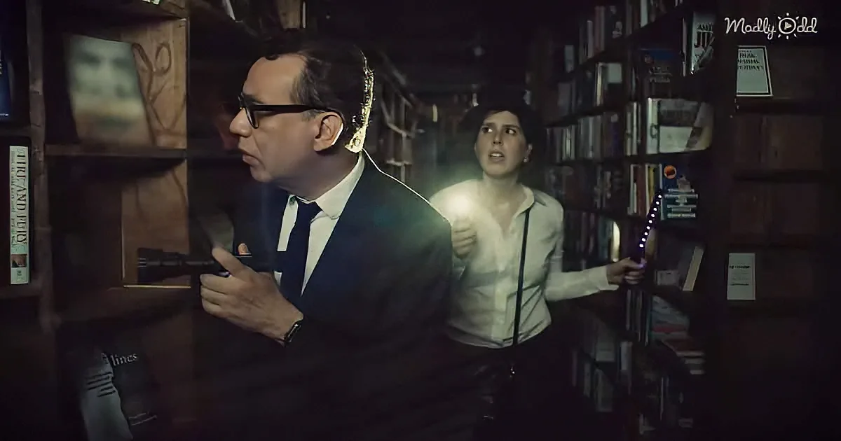 A man in a suit holds a gun, while a woman with a flashlight looks on in a dimly lit bookstore.