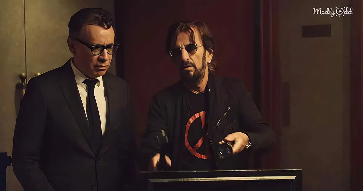 Two men, one in a suit and the other in a black shirt with a red symbol, stand in a dimly lit room, examining something...