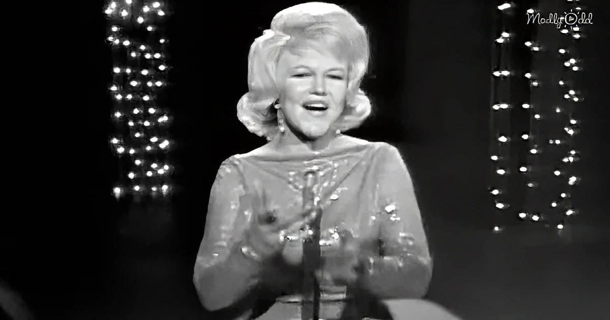 A woman in a sparkly dress holds a microphone, smiling, with lights in the background.