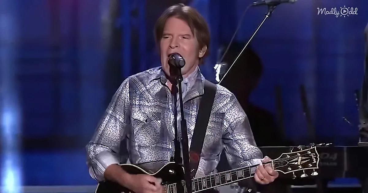 A man in a patterned shirt plays an electric guitar on stage, singing into a microphone.