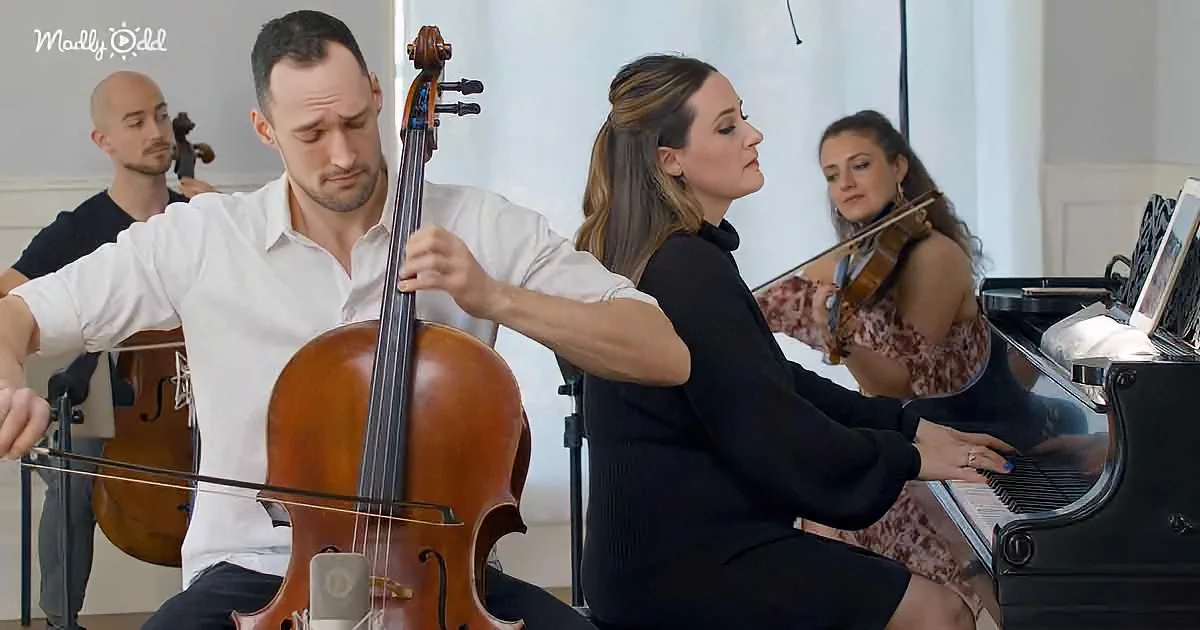 A man in white plays cello, surrounded by musicians in a performance setting.