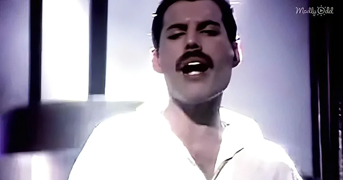 A person in a white shirt sings passionately, with a bright light source behind them.