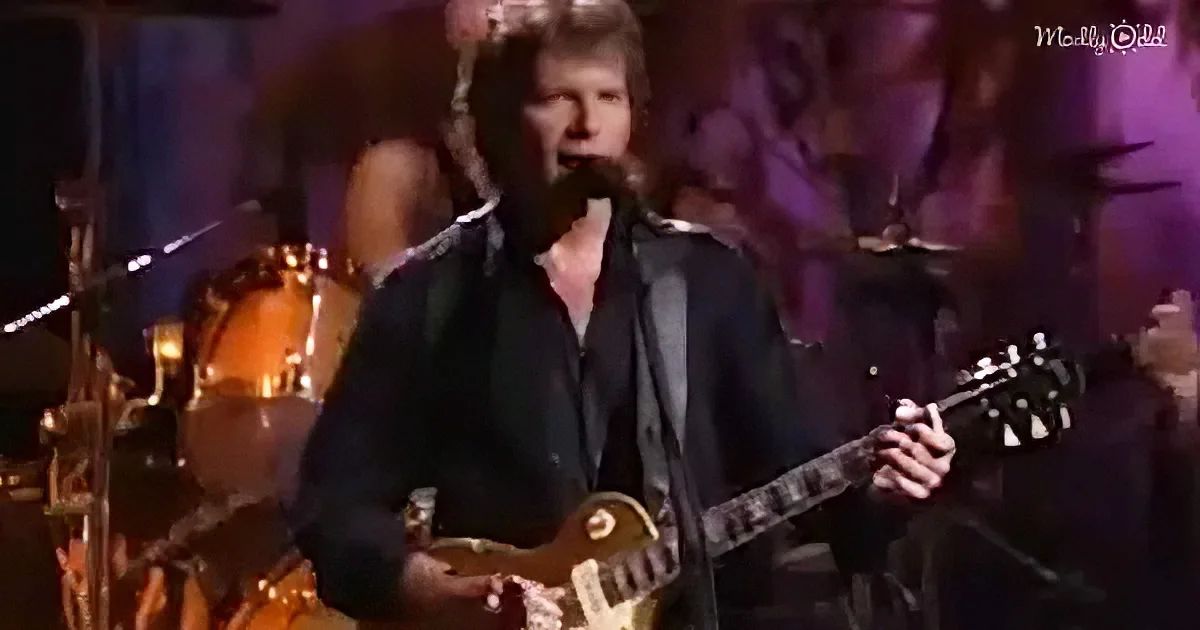 A man in a black leather jacket plays a guitar and sings into a microphone on stage.