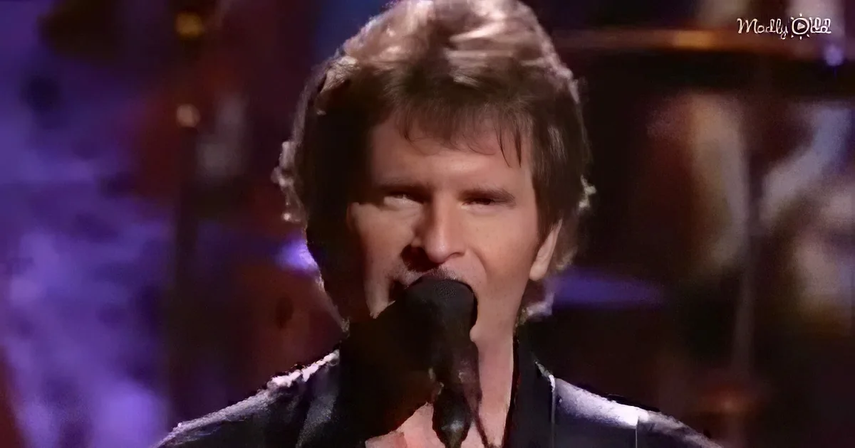 A man with blonde hair and a black suit sings into a microphone on stage.