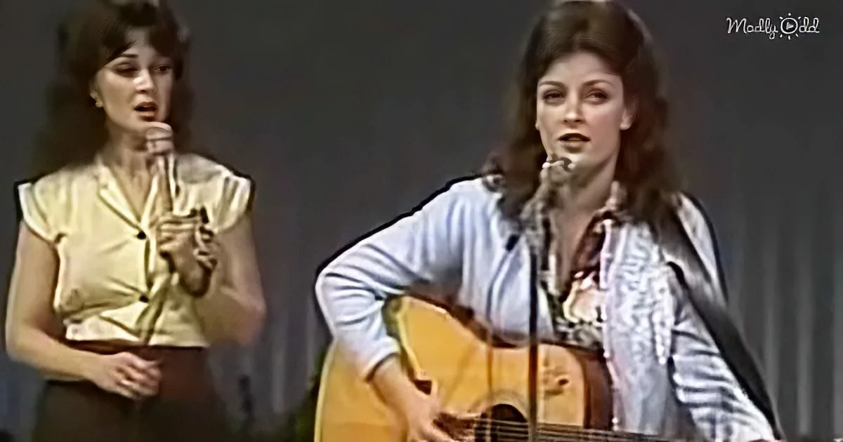 A woman in a yellow top sings into a microphone, another woman in a white jacket plays a guitar.