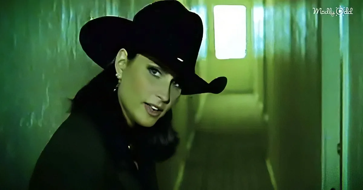 A person wearing a black hat and dark clothing stands in a dimly lit, green-hued hallway.
