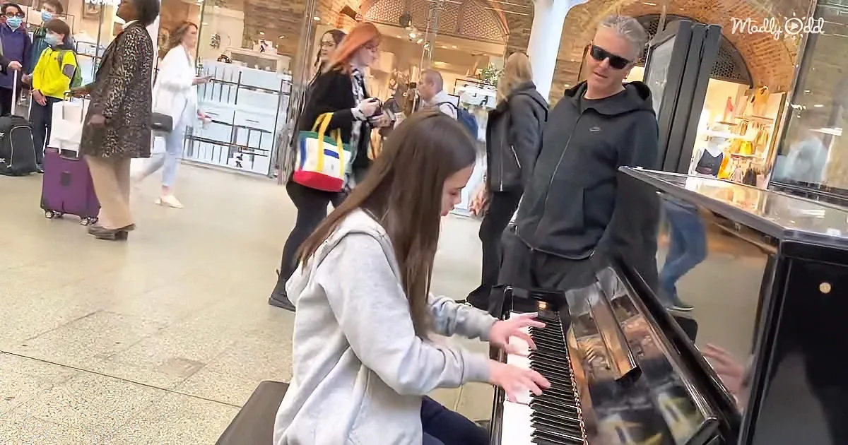 A young girl plays piano in a busy public space, surrounded by onlookers.
