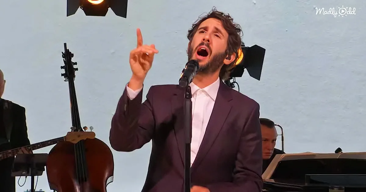 A man in a purple suit sings passionately, pointing upwards, with a cello and piano in the background.