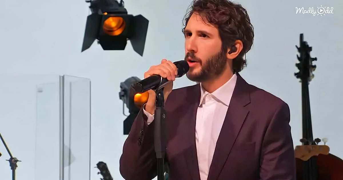 A man in a suit sings into a microphone, with stage lights and a bass guitar in the background.