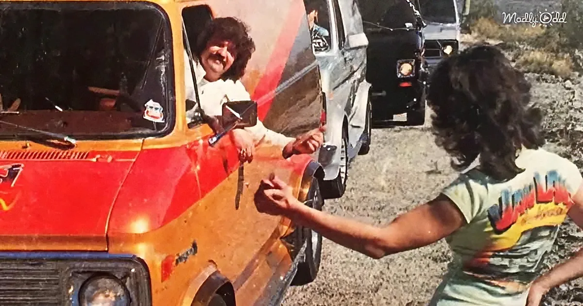 A man in a white shirt smiles from a red and yellow van, interacting with another person in a green shirt.