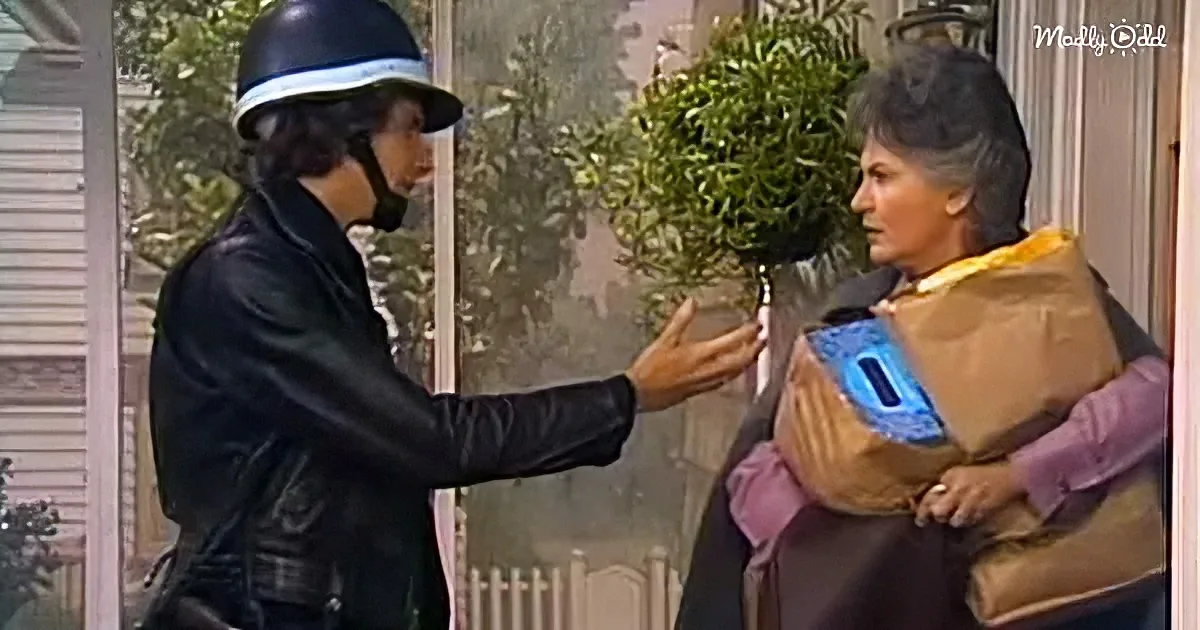 A person in a black leather jacket and helmet gestures towards another person holding a brown bag and a blue object.