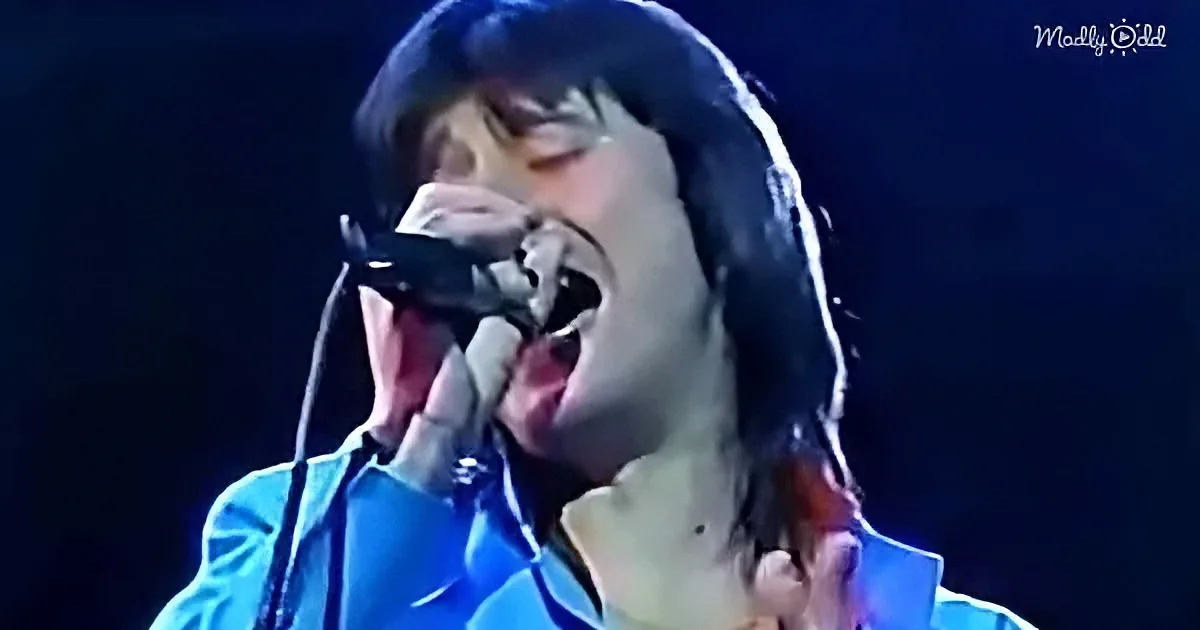 A person in a blue shirt sings passionately into a microphone on stage.