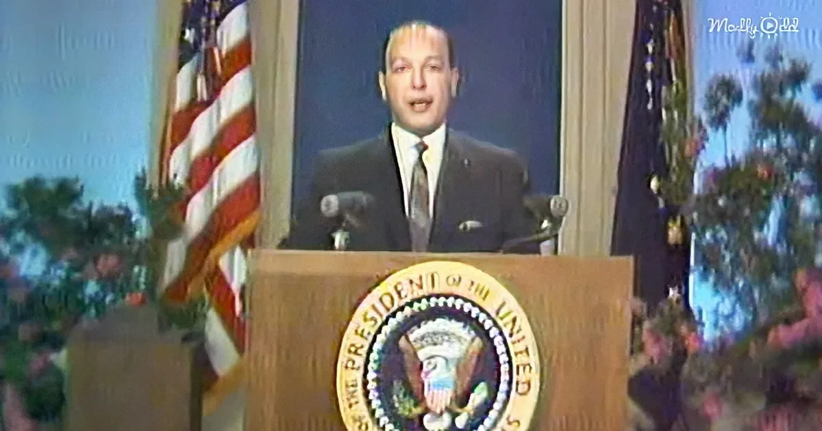 A man in a suit stands at a podium with the Presidential seal, speaking in front of an American flag.