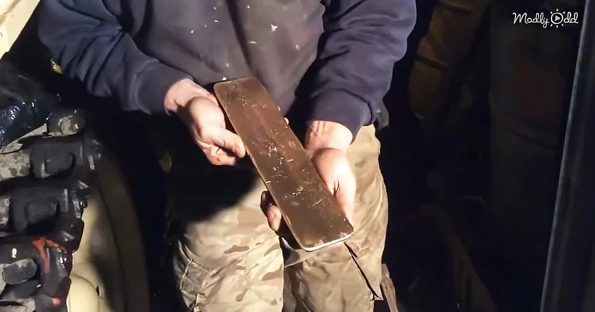 A person in a dark jacket holds a rusty metal object, possibly a tool or piece of equipment.