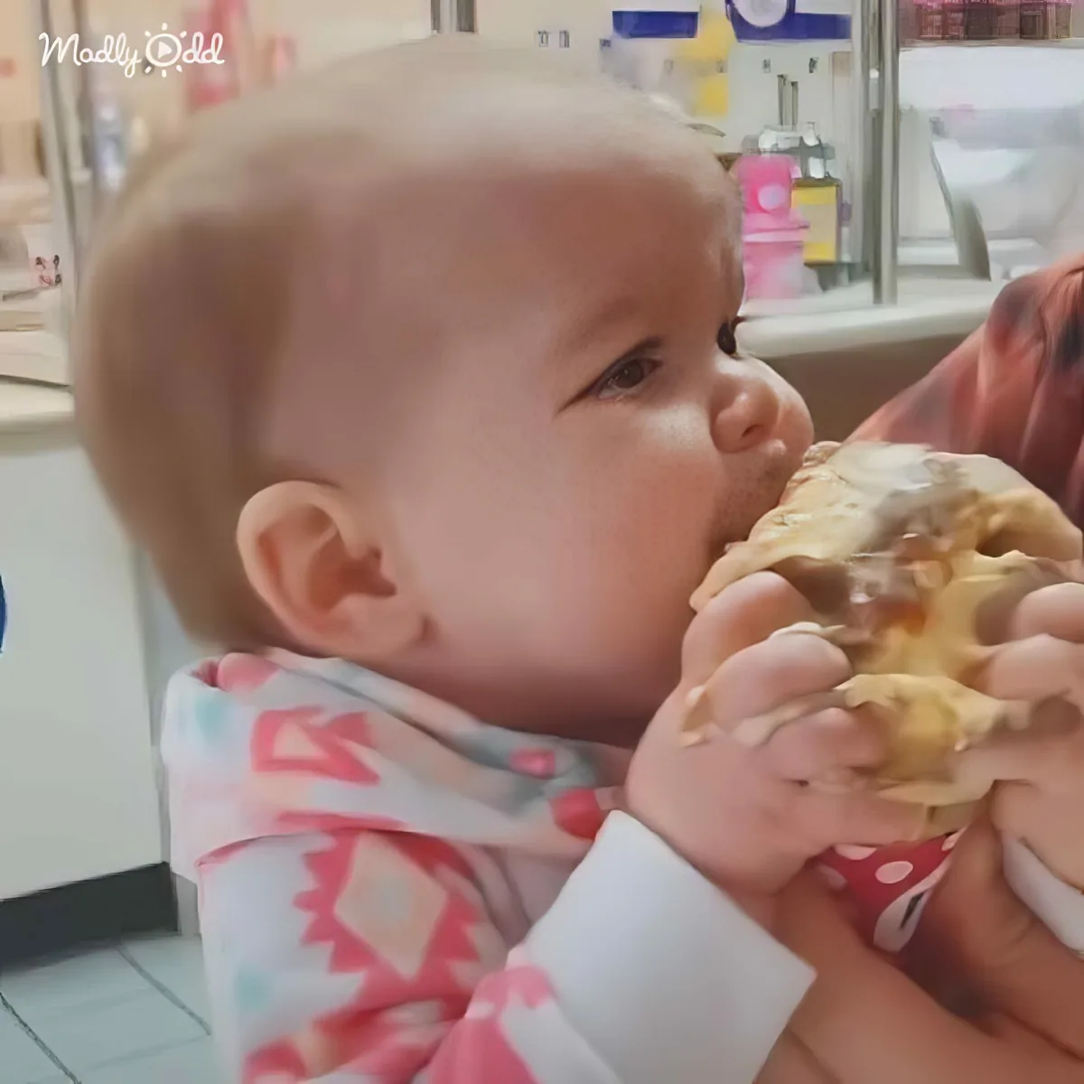 A baby in a bib is being fed a large piece of food by an adult.